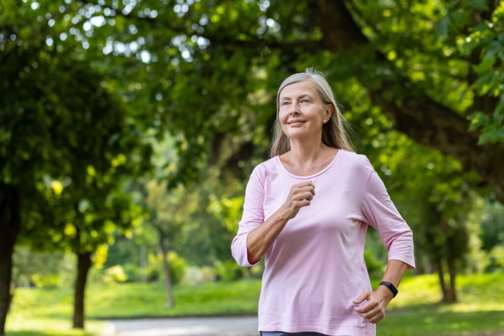 Senior mature woman running in the park on a sunny day, gray-haired sportswoman in sportswear happy